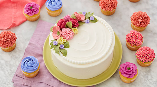Three cakes decorated with buttercream peonies, roses, and dogwood flowers