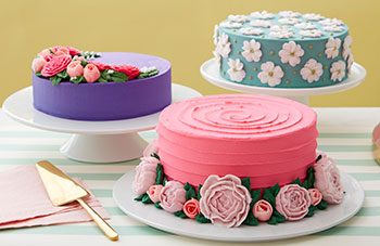 Three cakes decorated with buttercream peonies, roses, and dogwood flowers